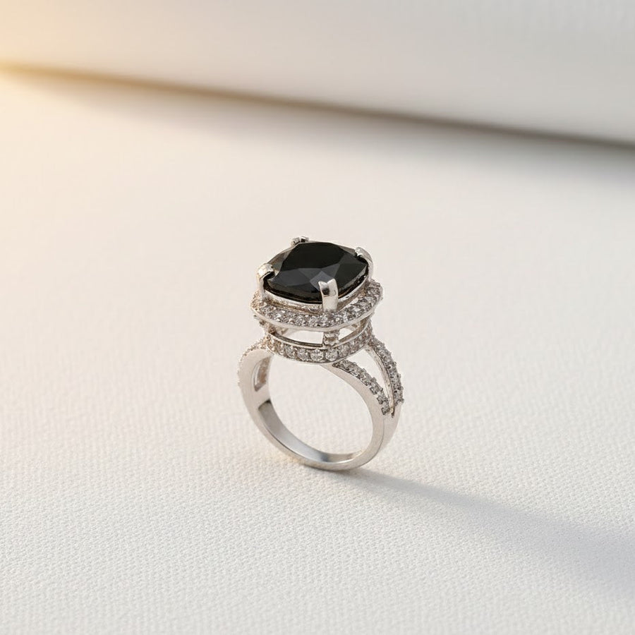 Black cushion-cut gemstone ring with double pavé halo and split silver-tone band on light background