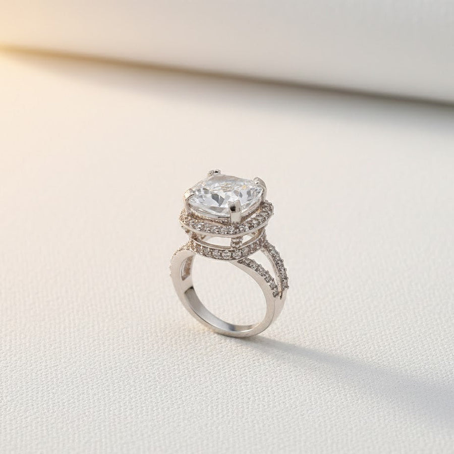 Cushion-cut clear gemstone ring with double pavé halo and split silver-tone band on light background