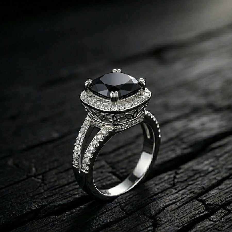 Close-up of cushion-cut black gemstone ring with double pavé halo and floral engravings on dark textured surface