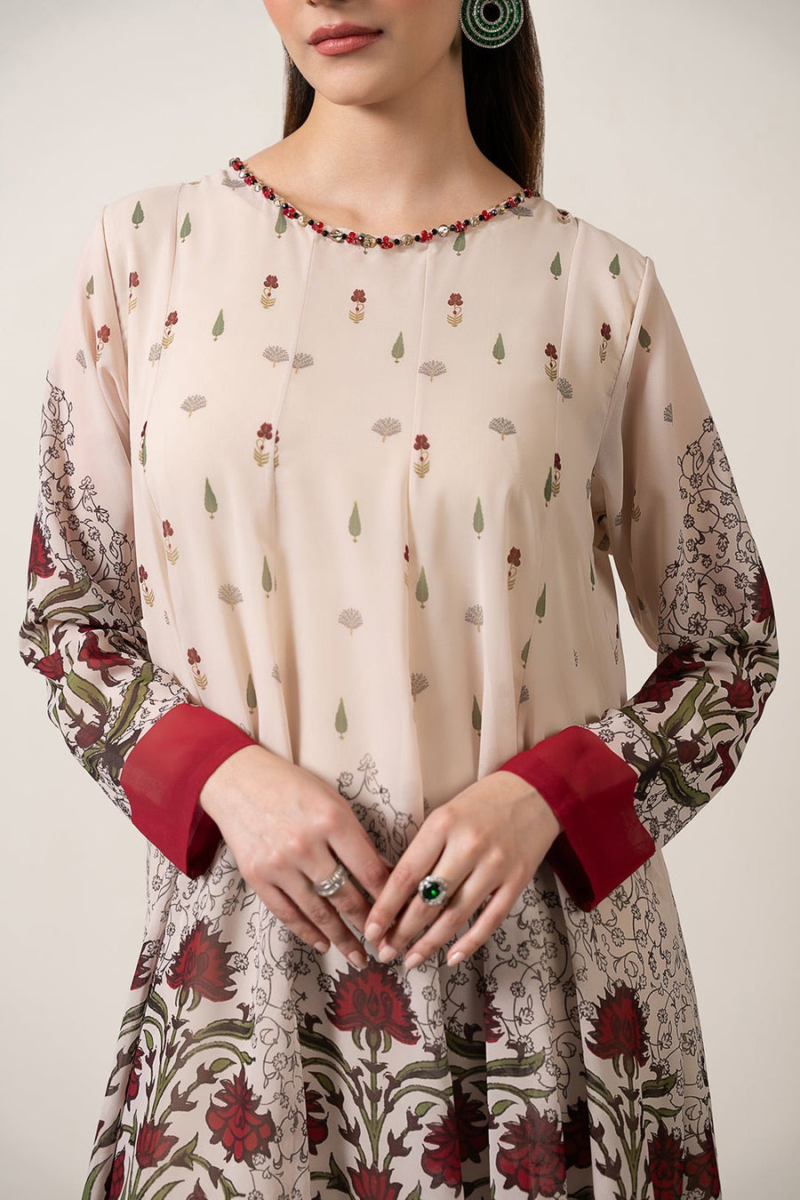 Close-up of embellished neckline and floral print detail on the chiffon pishwas dress with maroon cuffs and rings on model's fingers