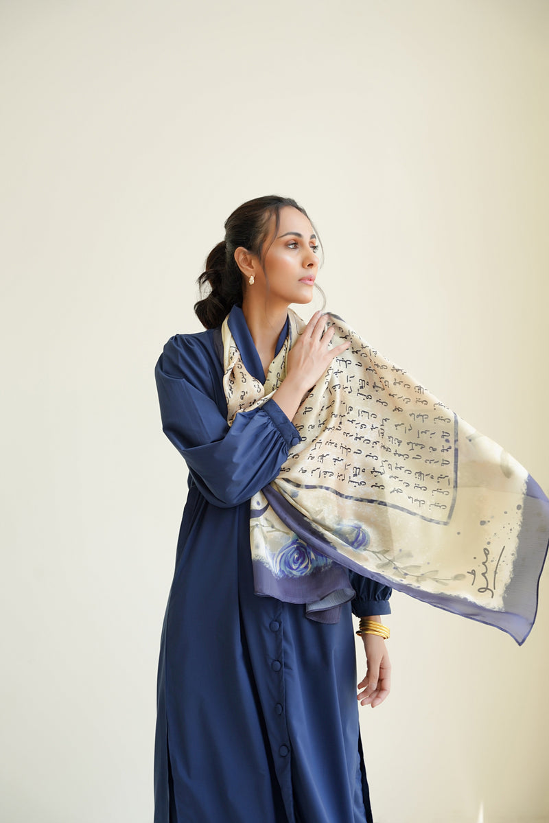 Woman wearing an elegant cream and navy blue scarf with artistic script and rose designs, styled with a navy blue dress.
