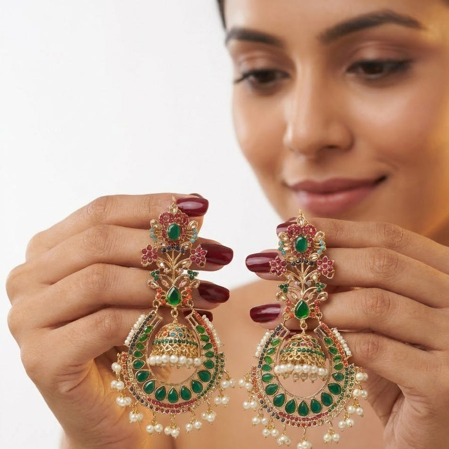 Woman holding green stone jhumka earrings with intricate detailing and pearl drops, demonstrating size and design