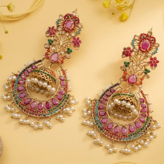 Close-up of exquisite traditional jhumka earrings with pink teardrop stones, multi-colored gems, and pearl drops on a warm yellow background