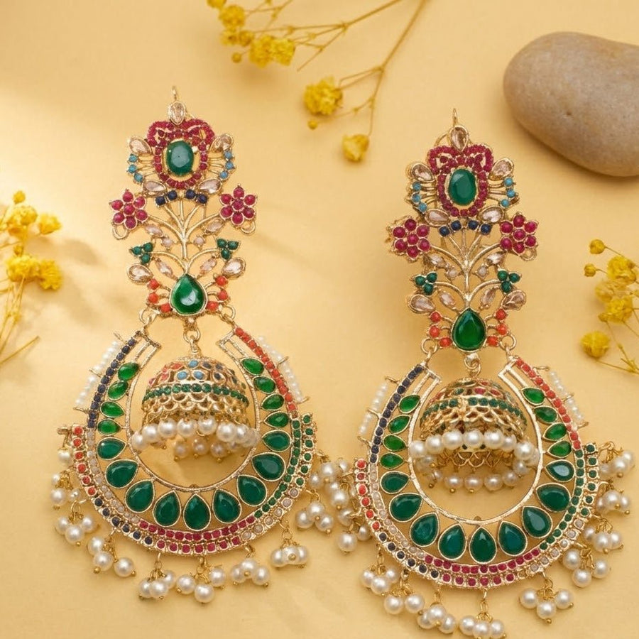 Traditional jhumka earrings with green stones and pearl embellishments displayed on a yellow background with decorative elements