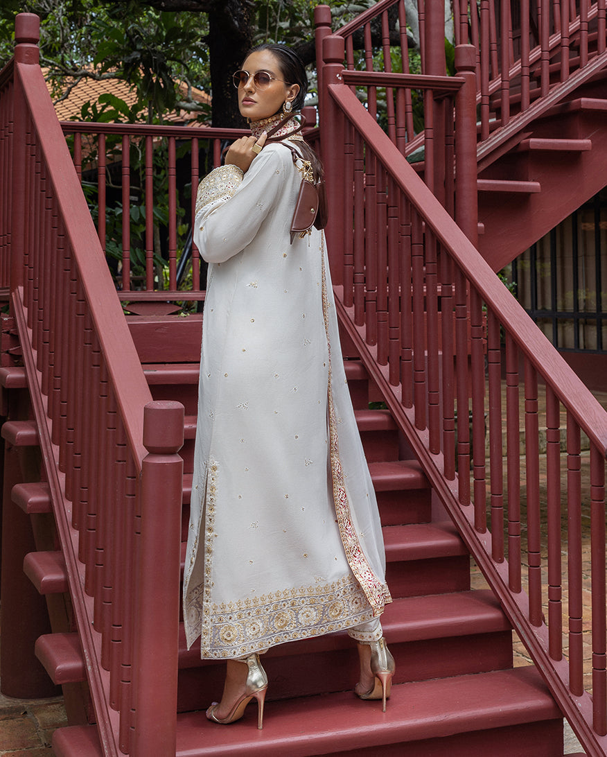 Back view of woman in embroidered ivory raw silk suit showing detailed embroidery along the back and sleeves, standing on red wooden stairs.
