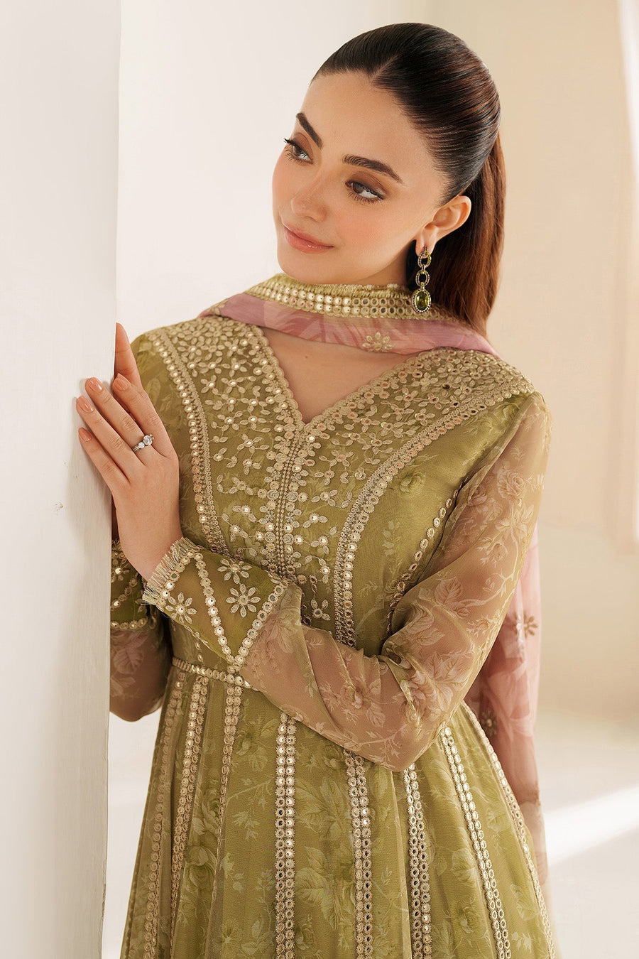 Portrait of woman smiling while looking downwards, wearing an olive green embroidered Anarkali dress with pink dupatta