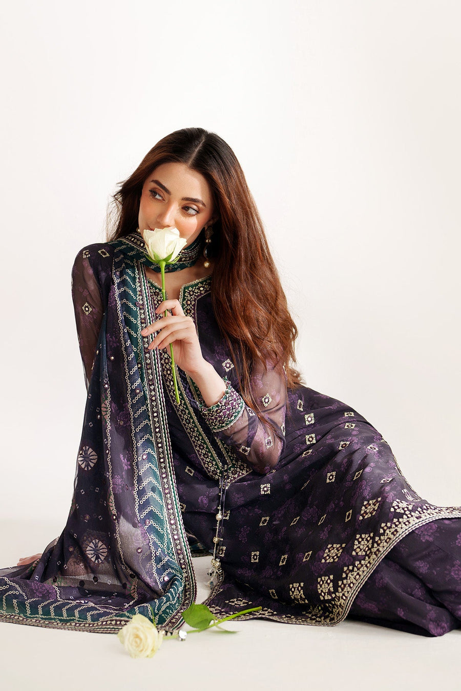 Model seated, holding a white rose, showcasing intricate embroidery and mirror work