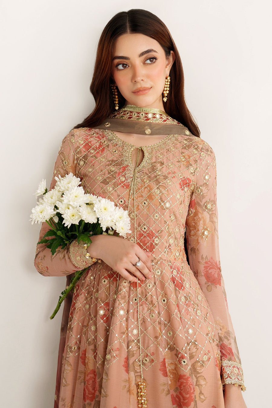 Half profile view of model in peach embroidered Anarkali suit looking out window