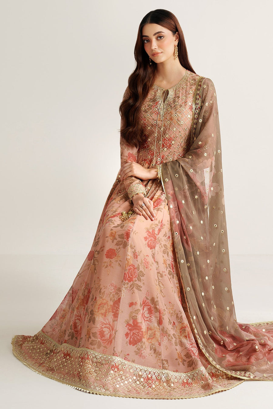 Seated pose of woman in luxury peach floral chiffon Anarkali suit with intricate gold embroidery