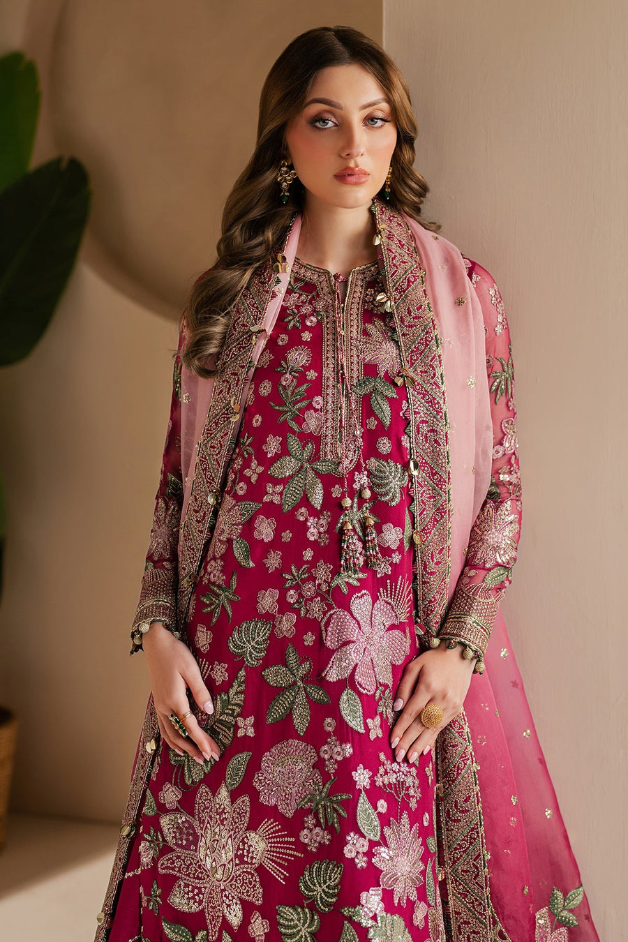 Model standing wearing deep magenta embroidered formal suit featuring decorative tassels and golden embroidered sleeves