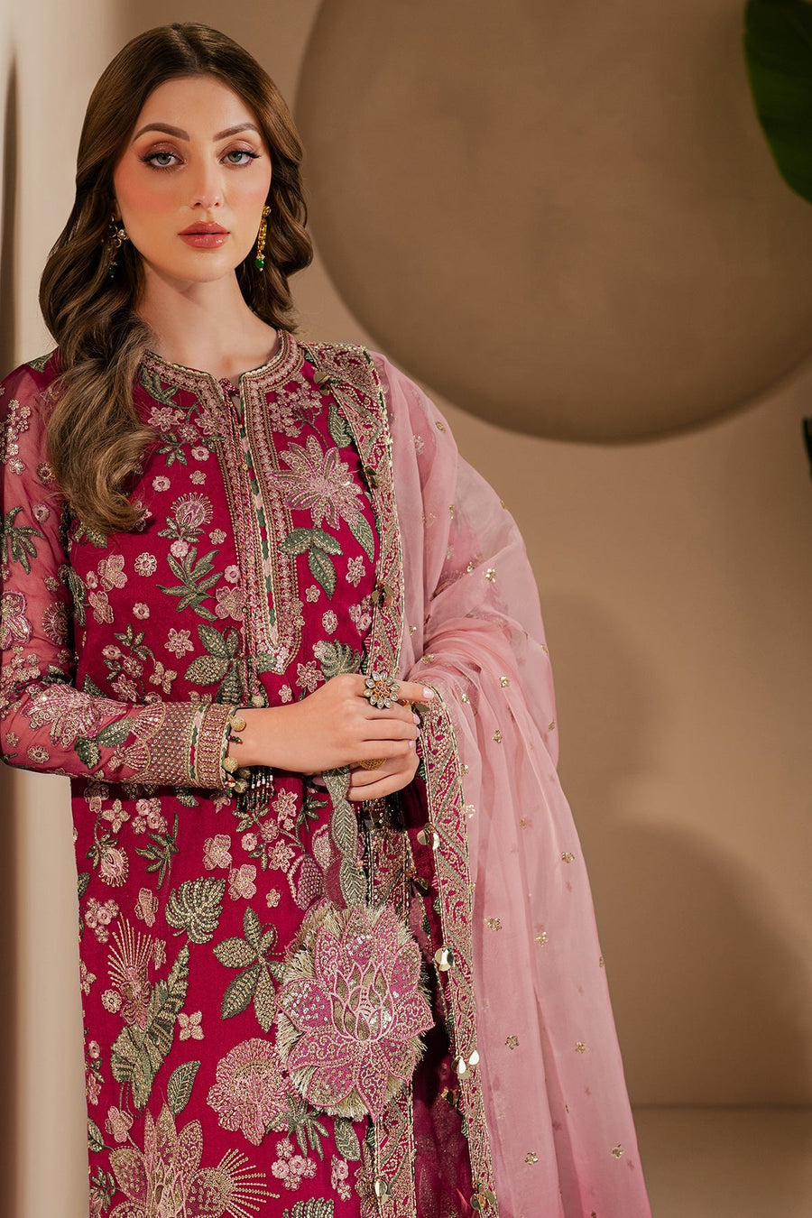 Elegant female model wearing deep magenta embroidered formal suit with sheer pink dupatta, showing rich fabric texture and fine embroidery