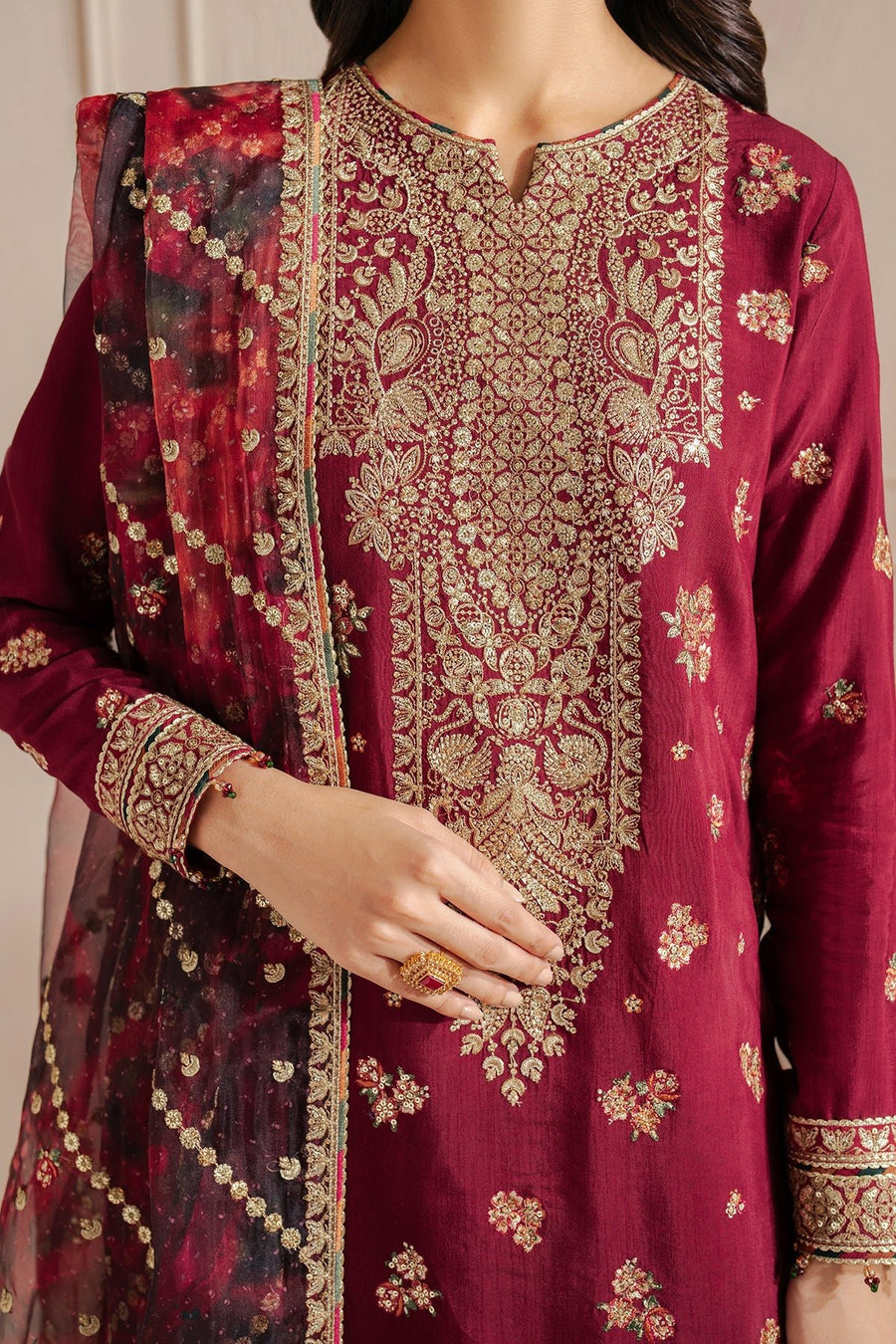 Close-up view focusing on the woman's crossed hands holding the maroon organza dupatta embroidered with gold sequins and bead tassels, detailing the precise craftsmanship and rich textures of the ensemble.
