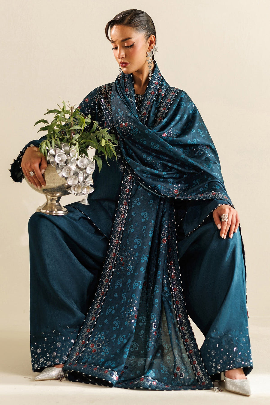 Close-up image of woman holding decorative silver bowl, showing embroidery details of the suit and accessories.