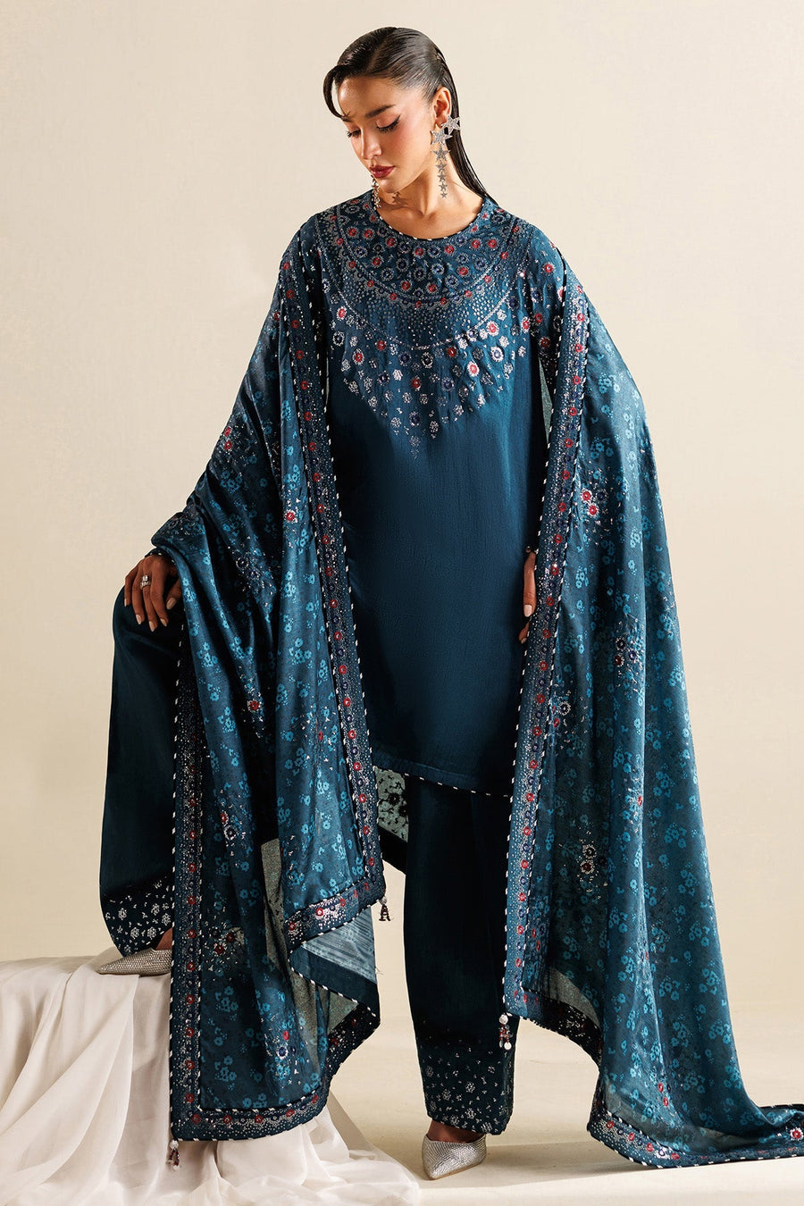 Woman wearing teal embroidered unstitched suit with detailed embroidery on neckline and sleeves holding the matching printed shawl.