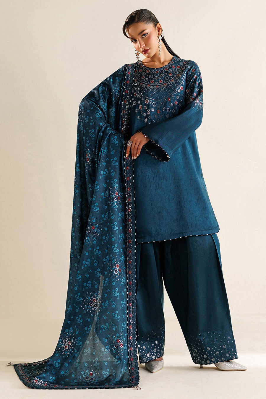 Woman sitting holding printed dupatta draped elegantly, showcasing detailed embroidery on border and trouser hem.