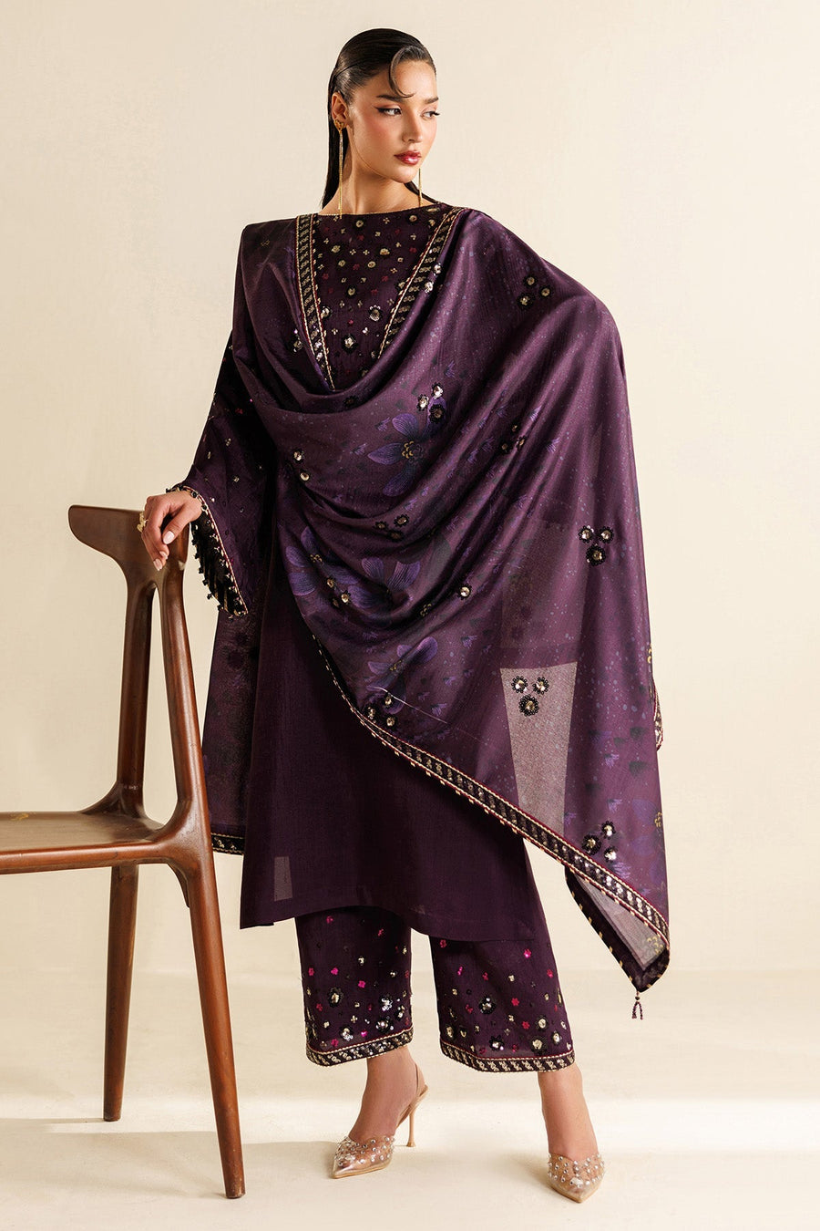 Woman wearing deep plum embroidered raw silk suit with floral motifs, posing by a wooden chair