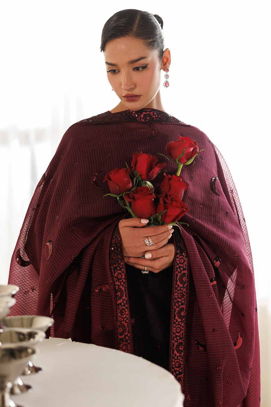 Elegant black embroidered kameez paired with wide-legged trousers with embroidered cuffs and sheer maroon crescent embroidered dupatta styled over both arms.