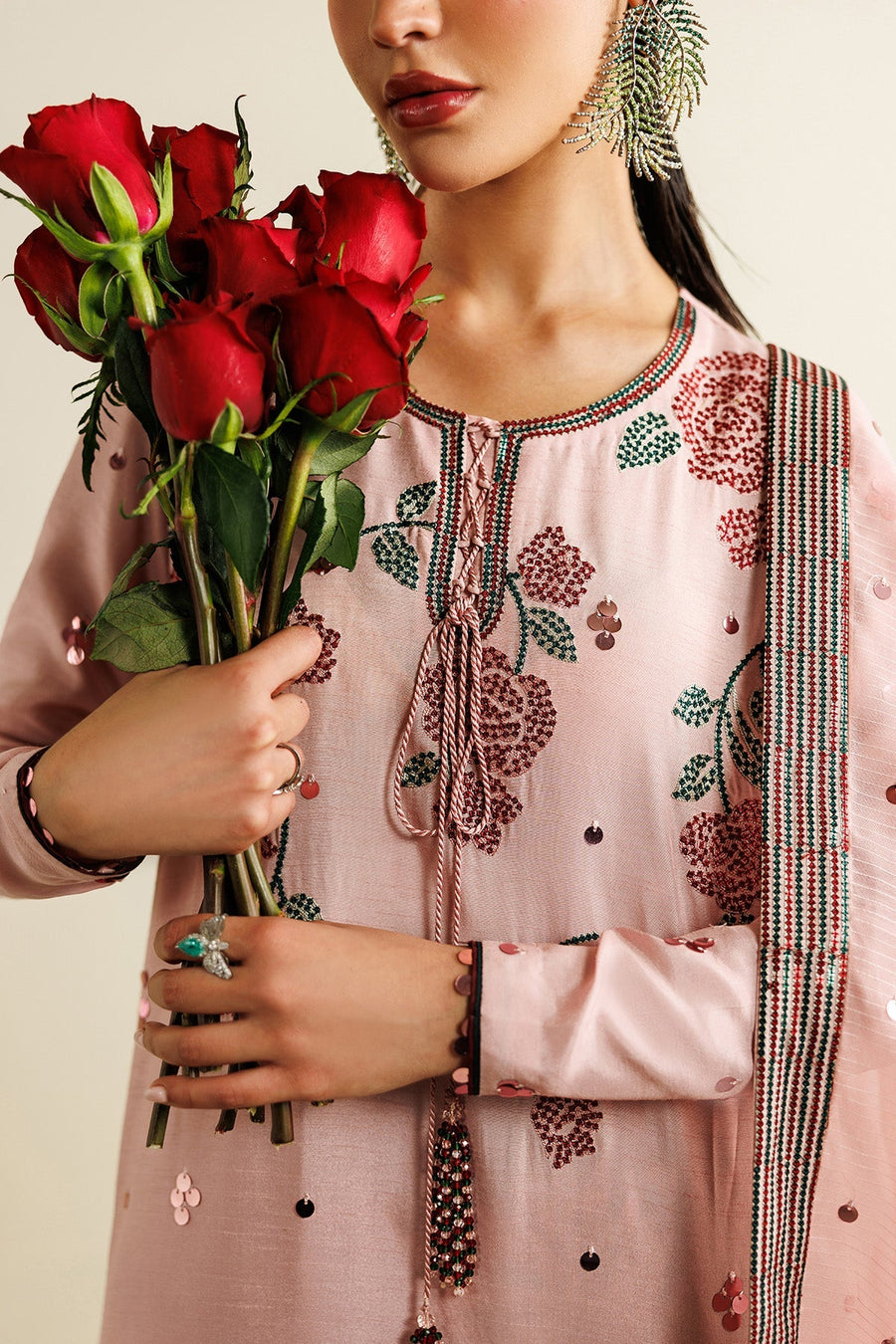 Model adjusting her dupatta draped over pastel pink embroidered suit with sequin detailing and red floral pants