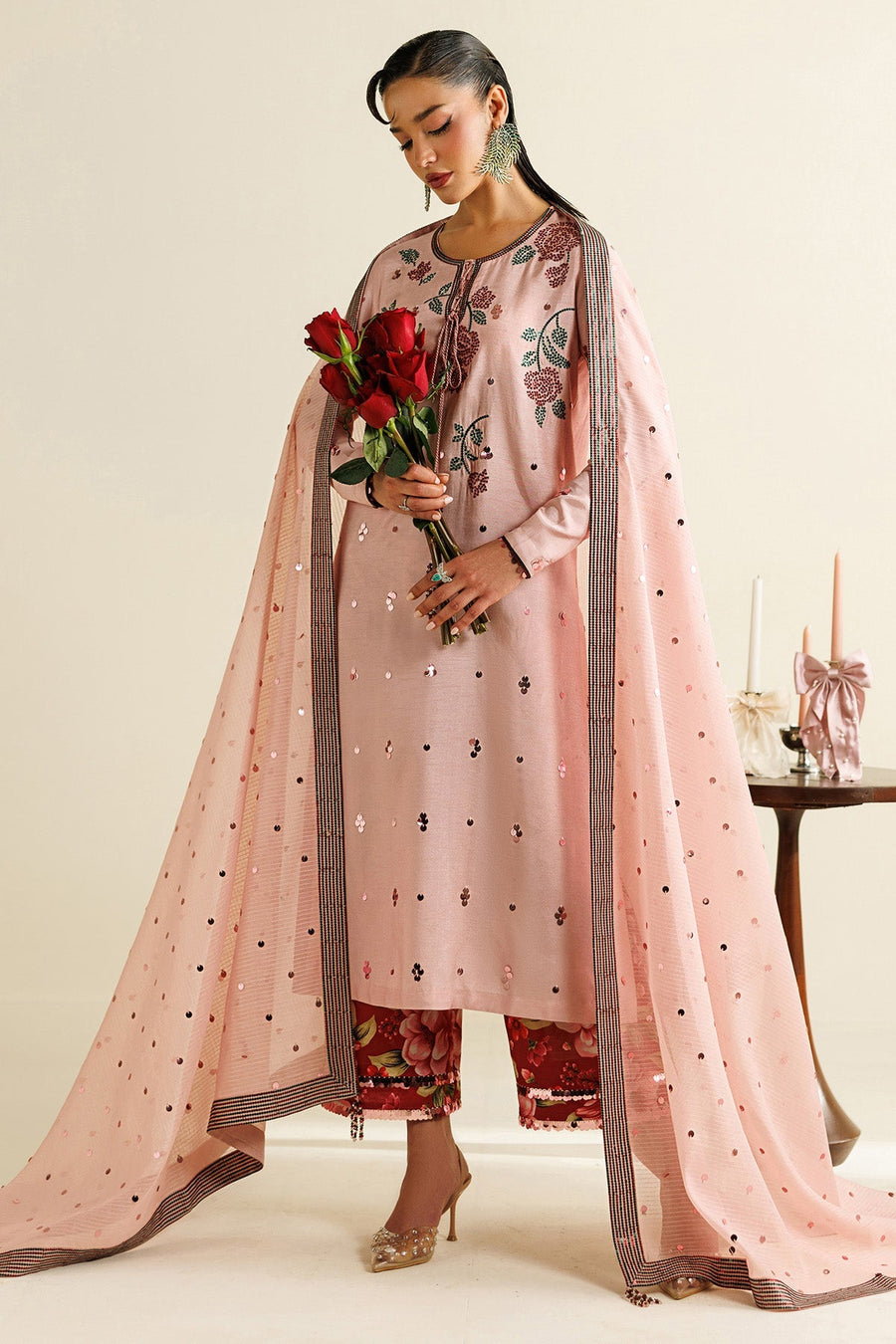 Close-up detail of embroidered floral and sequin work on pastel pink fabric with red roses held by model