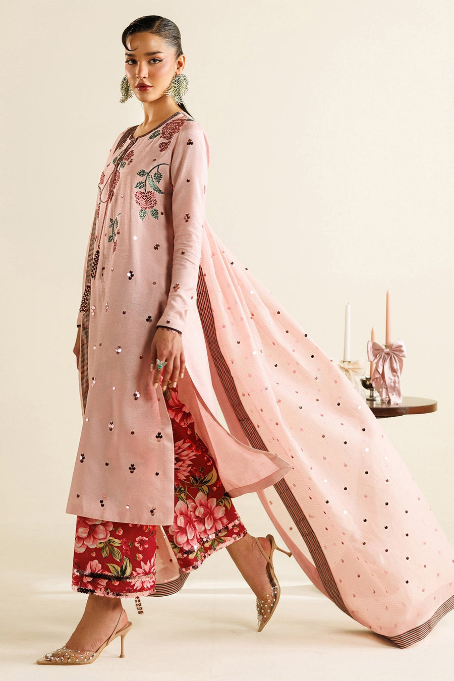 Woman modeling embroidered pastel pink unstitched suit with floral embroidery, sequin embellishments, red floral pants and long matching dupatta