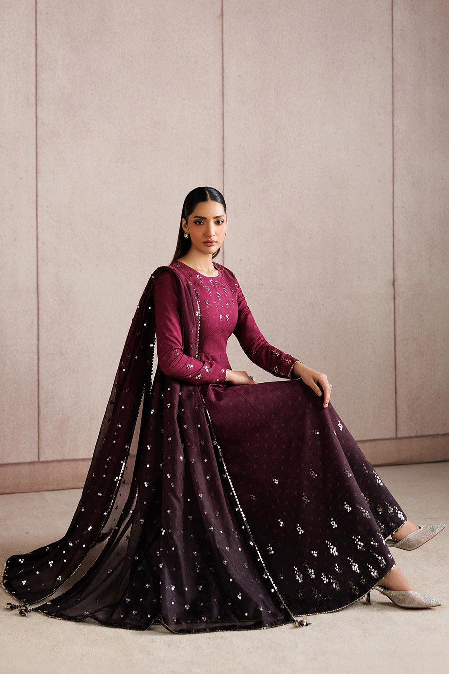 Woman seated wearing deep magenta Anarkali suit with sequin embroidery and matching tasseled dupatta