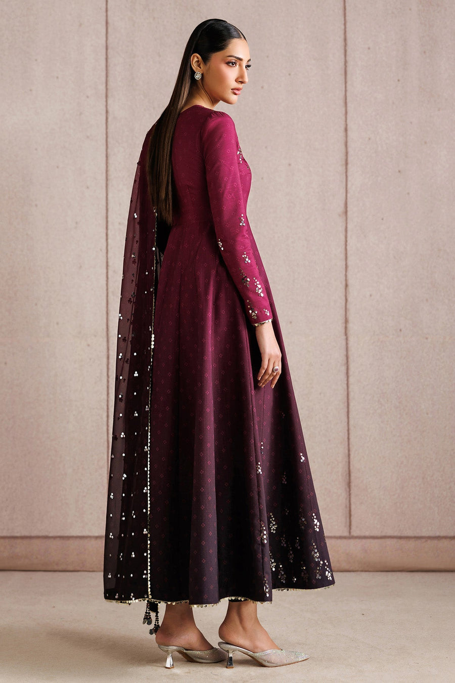 Side view of woman modeling full-length embroidered deep magenta Anarkali dress with fitted bodice and flowing skirt