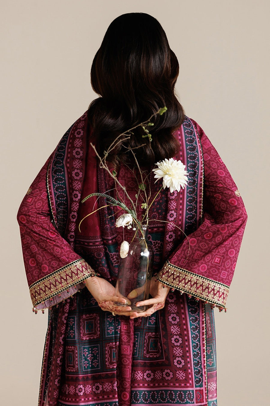 Back view close-up of model holding glass vase behind back with deep magenta embroidered dupatta wrapped around, highlighting print and embroidery details.