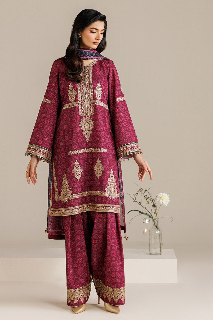 Back view of model showcasing embroidered deep magenta suit with detailed embroidery and matching dupatta draped over shoulder, against minimalist background.