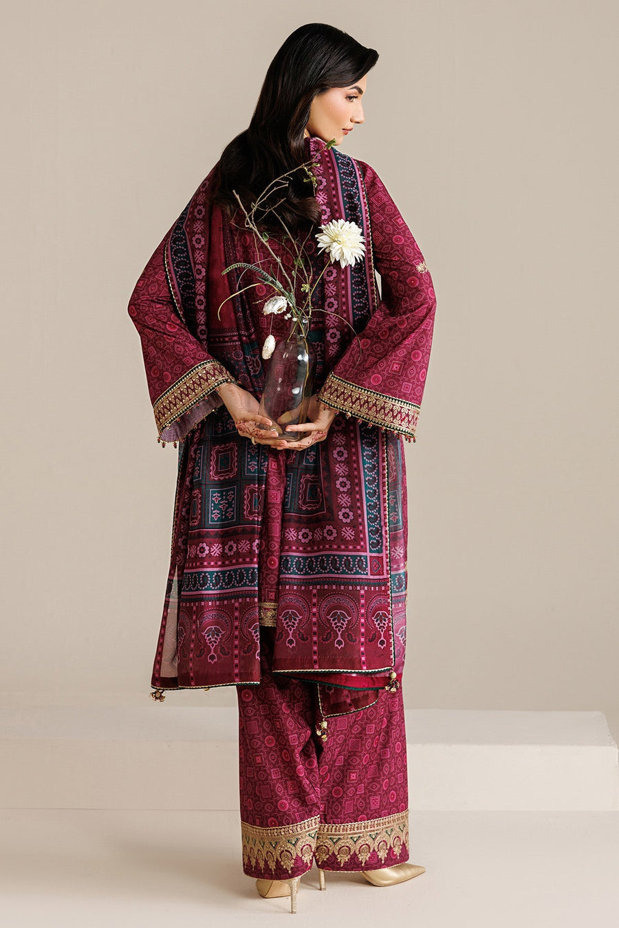 Model from front leaning on chair, wearing deep magenta embroidered suit with detailed neckline and sleeve embroidery, showcasing fabric quality and design.