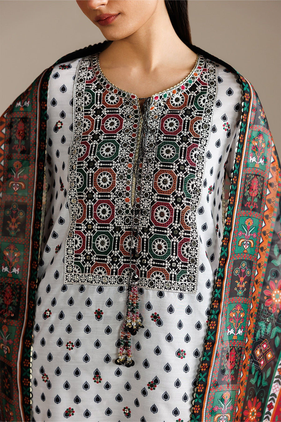 Detailed close-up of embroidery on white lawn fabric neckline showing geometric patterns and small embroidered sequins, complemented by printed dupatta.