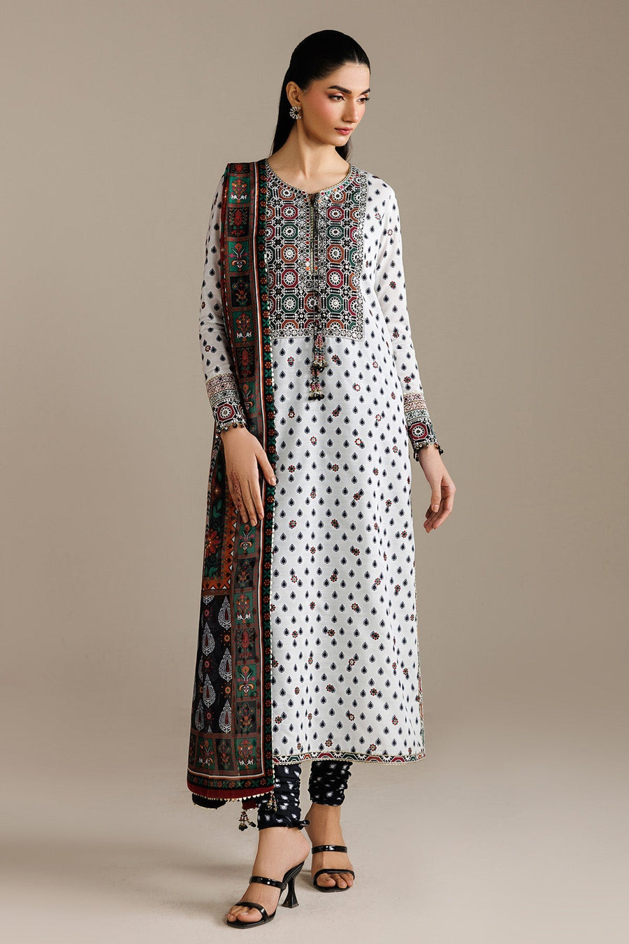 Woman wearing white embroidered lawn kurta with detailed embroidery on neckline and cuffs, paired with a printed multi-color dupatta and black printed trousers.