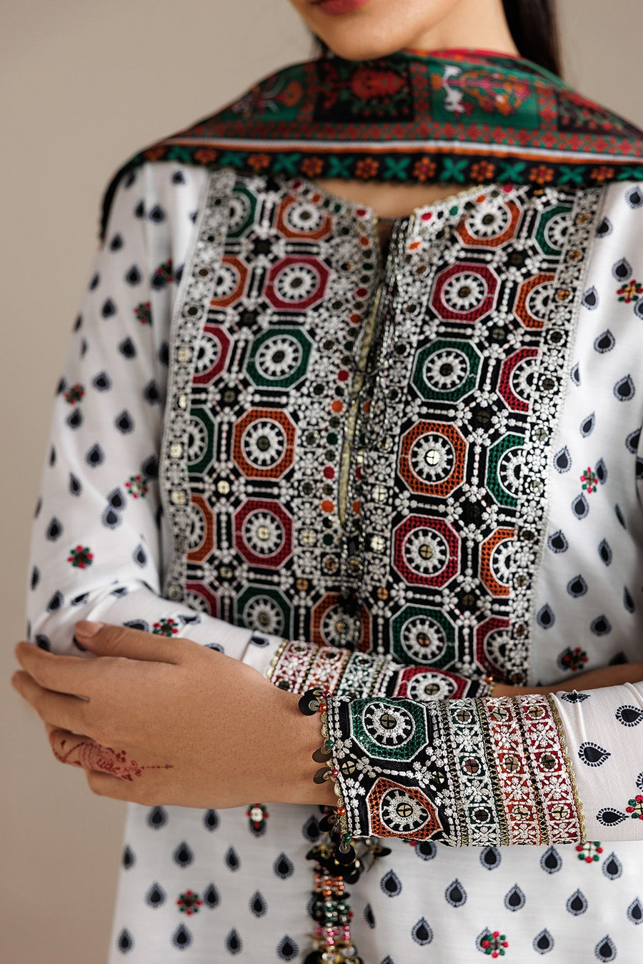 Full-length portrait of woman wearing embroidered white lawn suit with vibrant printed dupatta featuring geometric and floral motifs.