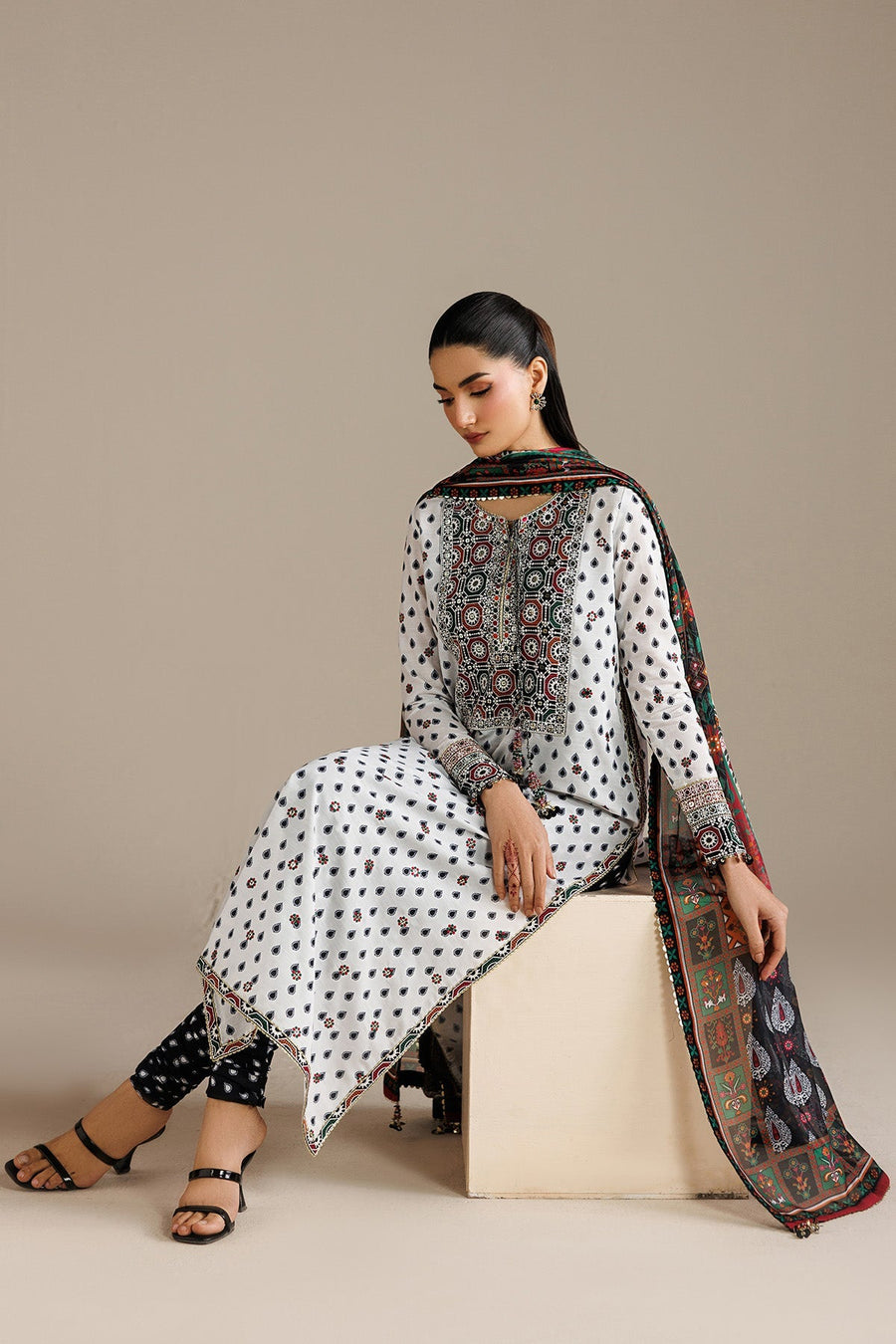 Close-up of woman’s upper body displaying intricate embroidery on neckline and cuffs of white lawn kurta with printed multi-color dupatta.
