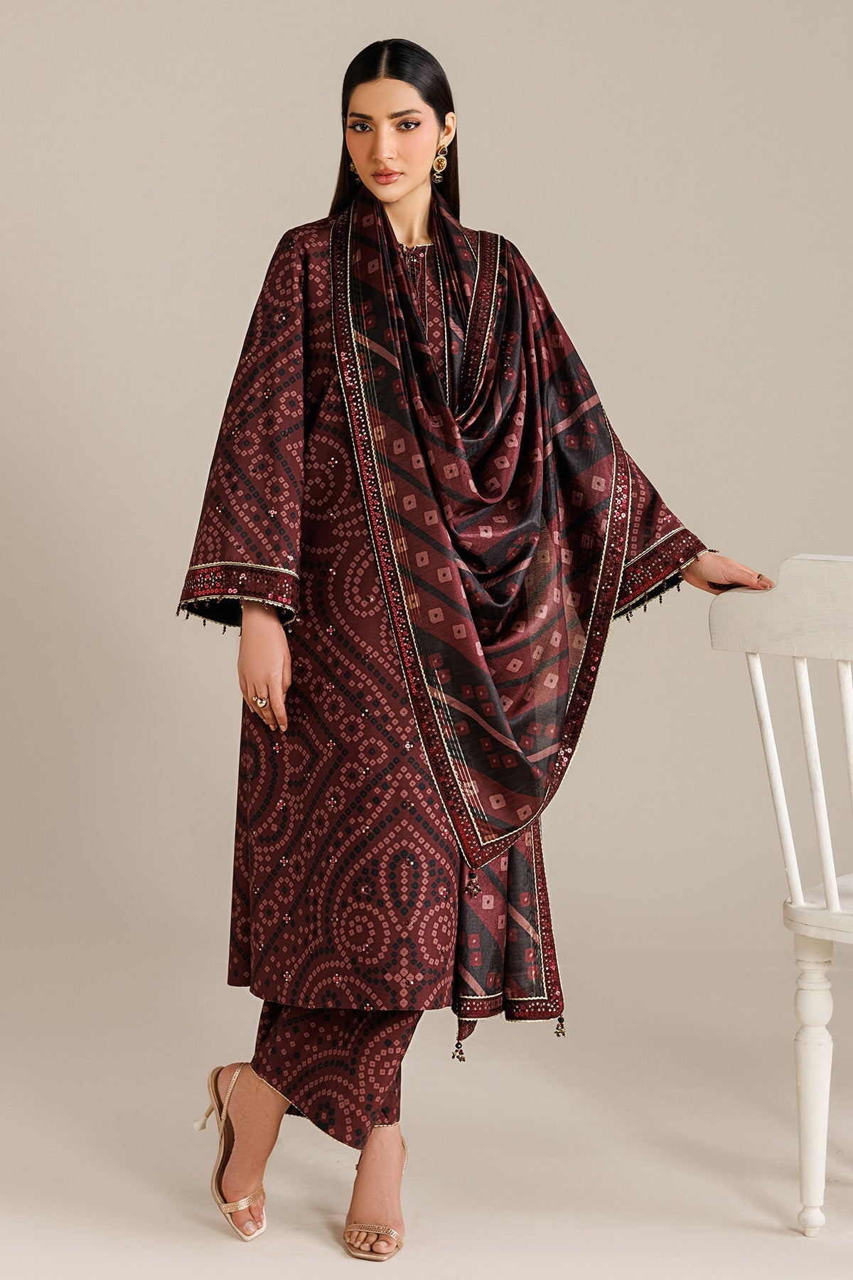 Woman in full view wearing an embroidered raw silk suit with a coordinated maroon and black printed dupatta draped on her shoulder, showcasing sequin-trimmed sleeve borders.