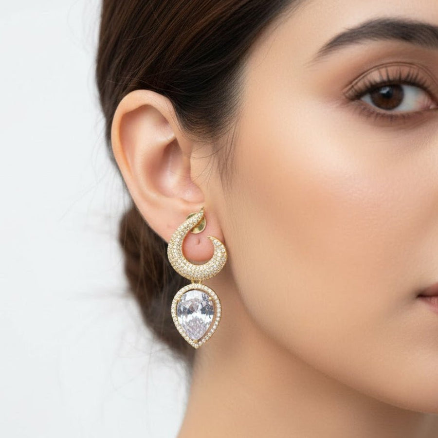 Gold-plated earrings with clear teardrop stones worn by a woman showing side profile