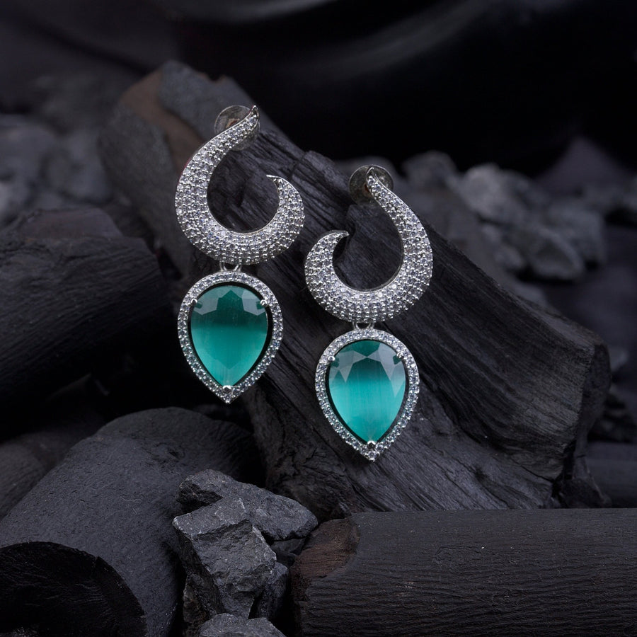 Silver-plated earrings with green teardrop gemstones placed on black charcoal pieces