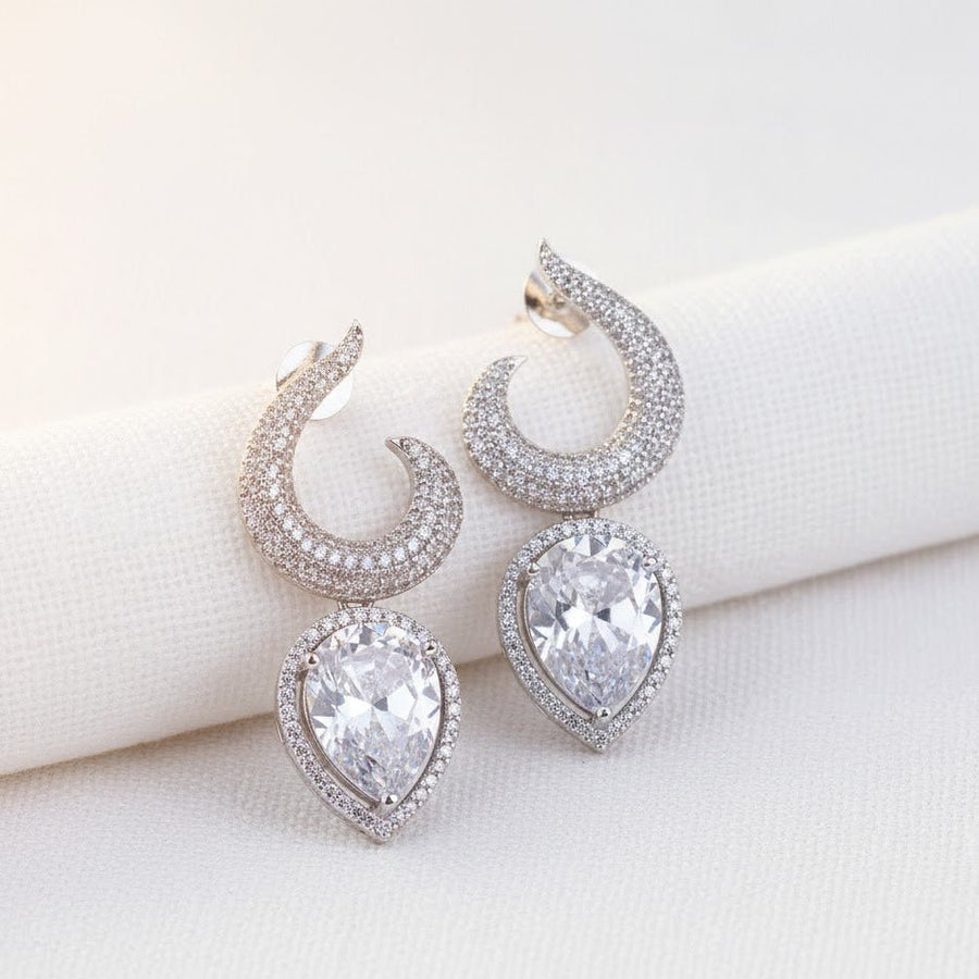 Silver-plated earrings with clear teardrop gemstones displayed on white fabric