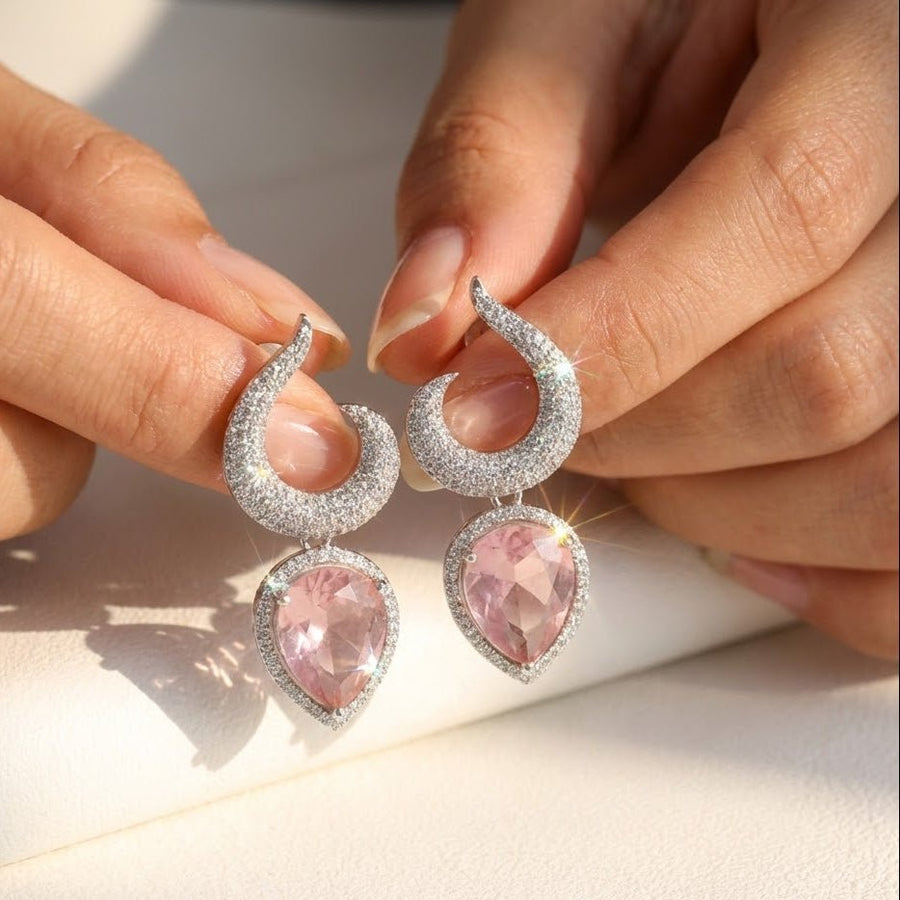 Gold-plated earrings with pink teardrop gemstones displayed on white fabric with soft lighting