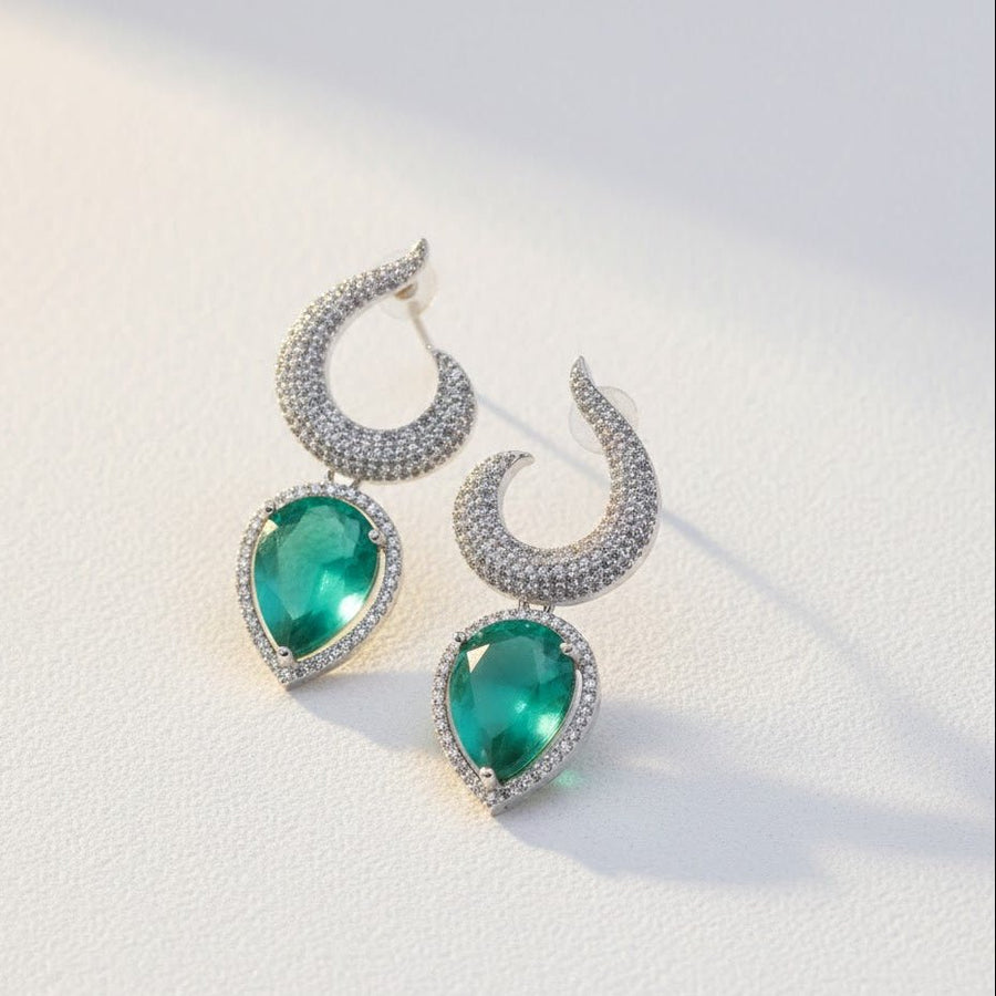Hand holding silver-plated earrings with clear teardrop gemstones against outdoor sunlight
