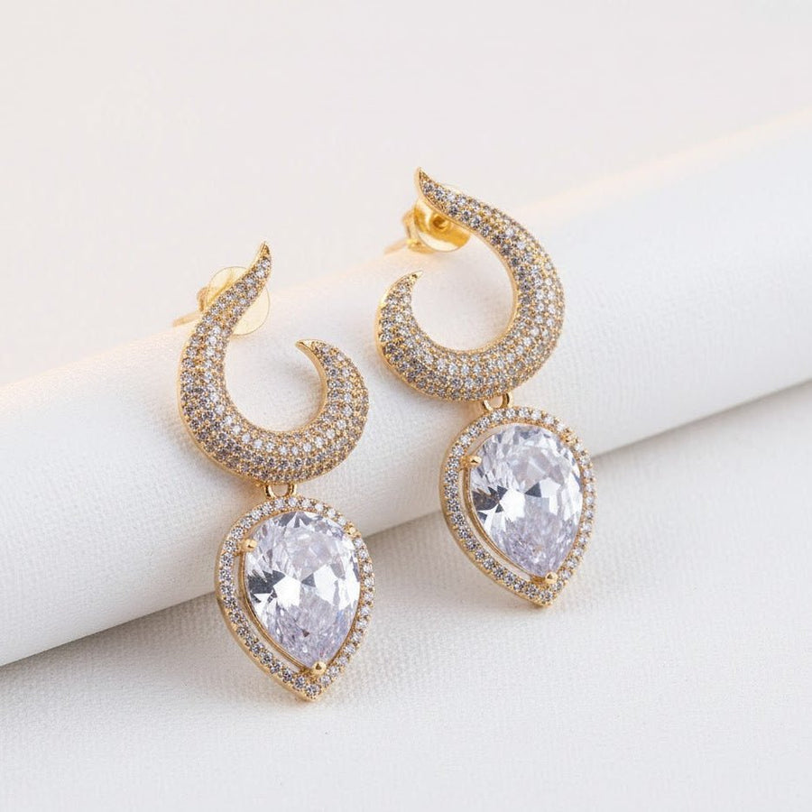 Gold-plated earrings with clear teardrop stones placed on soft white fabric