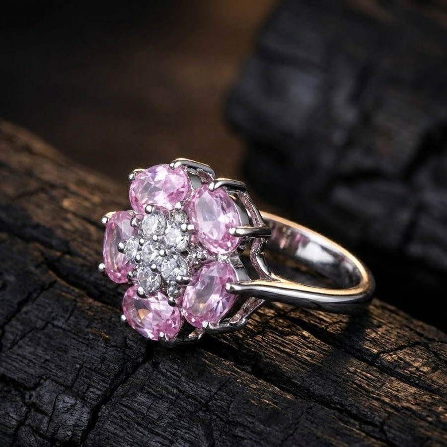 Silver floral ring with pink stones placed on textured black surface emphasizing sparkle and craftsmanship.
