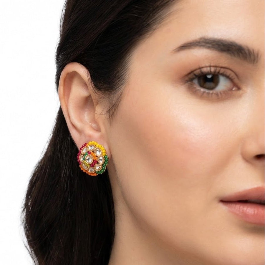 Close-up of a woman wearing round multi-color stud earrings with gold-plated detailing and clear Polki-style stones, highlighting the elegant fit and vibrant design