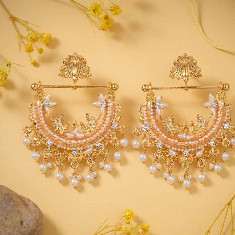 Gold-plated peach stone and pearl jhumka earrings displayed with yellow flowers and stones outdoors
