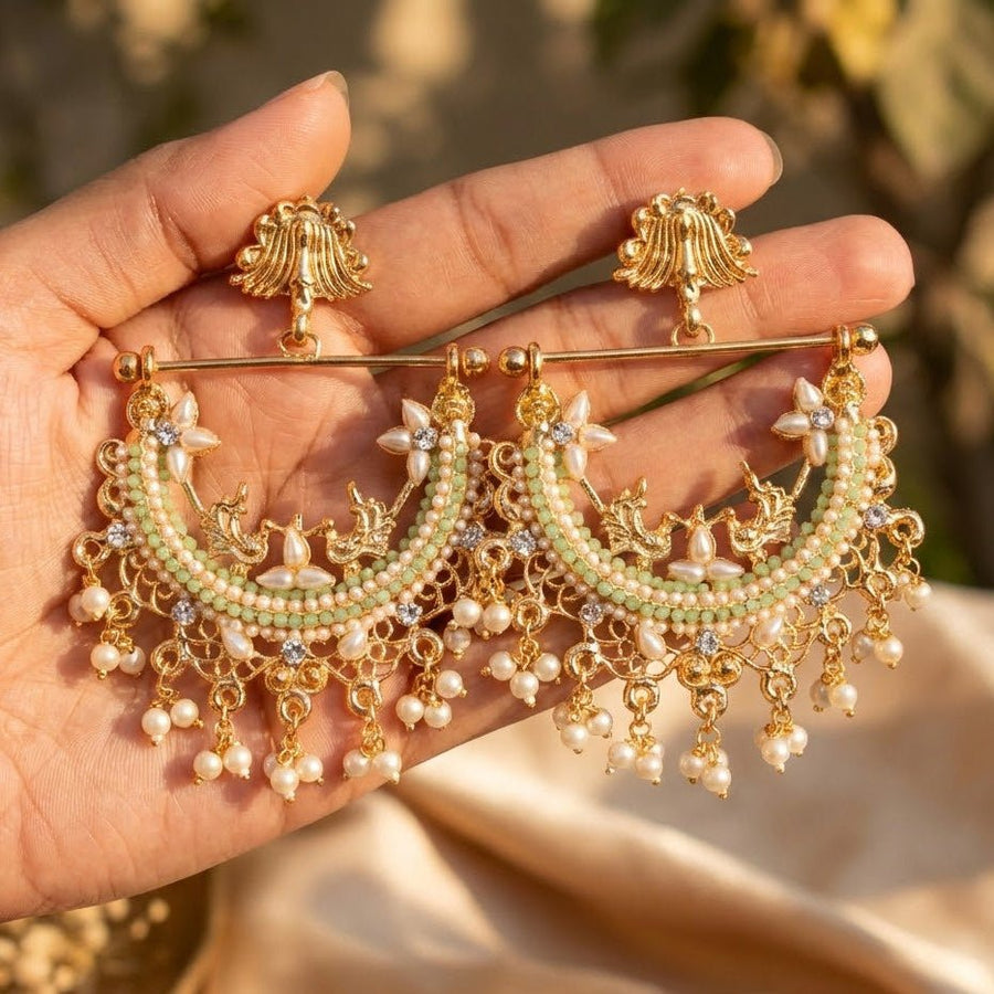 Hand holding mint green stone adorned gold-plated pearl jhumkas showing detailed design