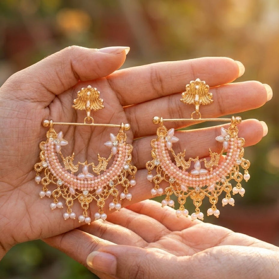 Hand holding mint green stone embellished gold-plated pearl jhumkas shown outdoors in sunlight