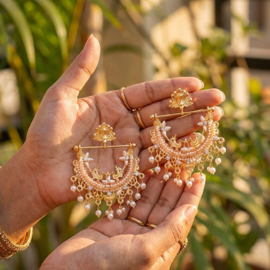 Hand holding peach stone adorned gold-plated pearl jhumka earrings in natural light