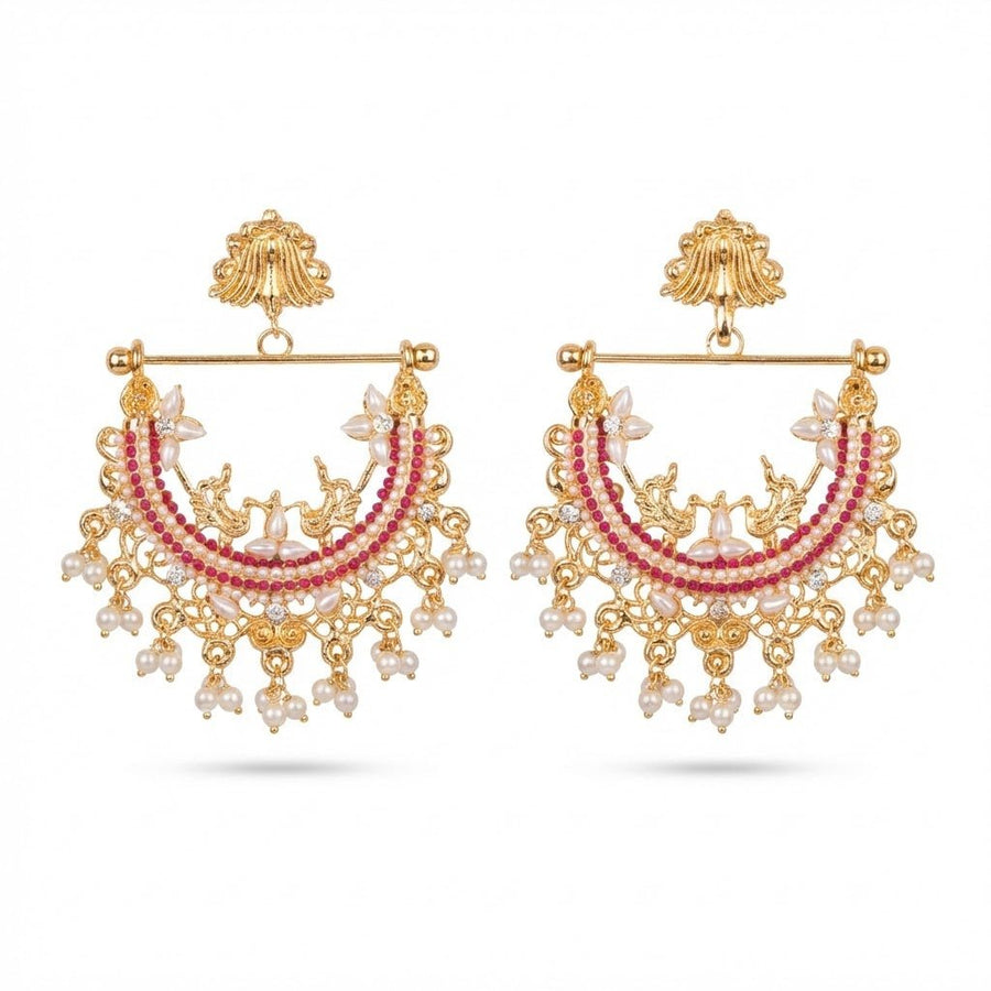 Close up of gold-plated jhumka earrings featuring red stones and elegant pearl drops on white background