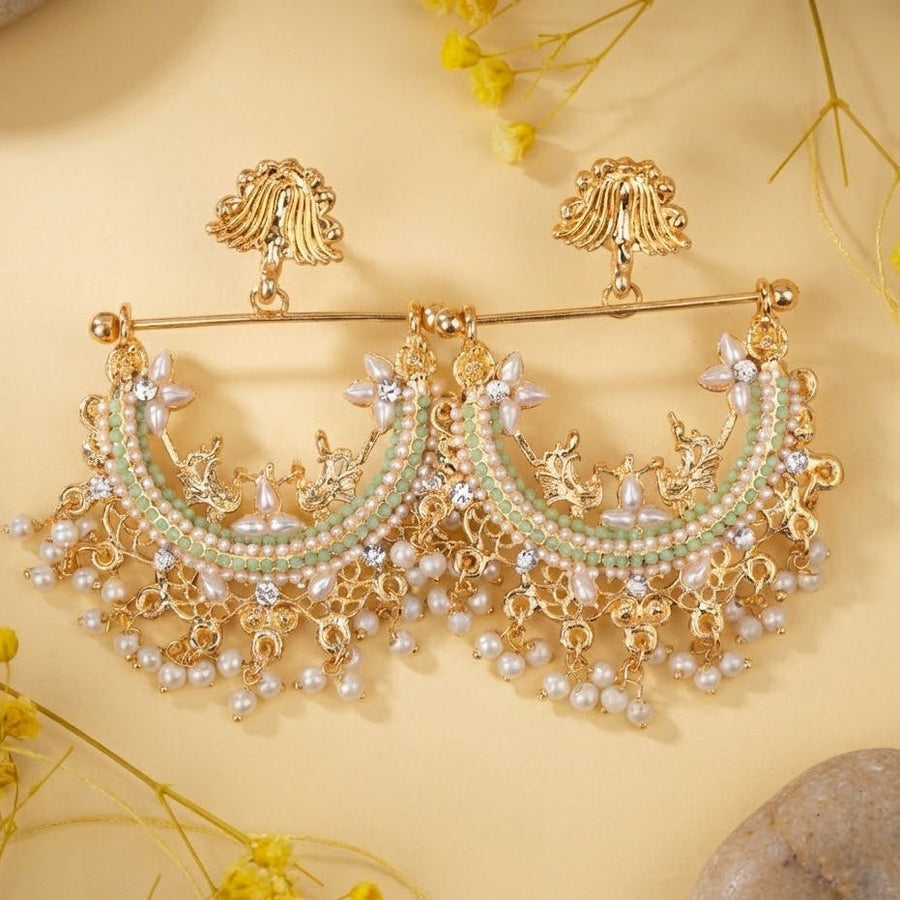 Gold-plated pearl jhumka earrings with mint green stones shown on cream background with stones