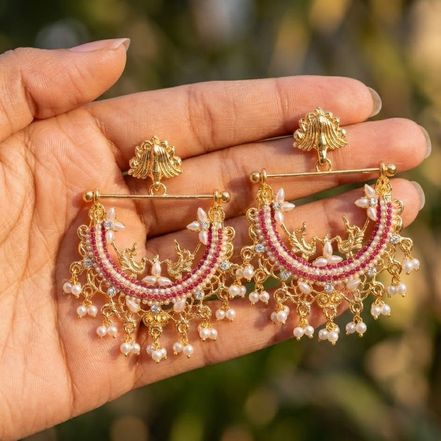 Hand holding red and gold pearl jhumka earrings showcasing detailed craftsmanship outdoors