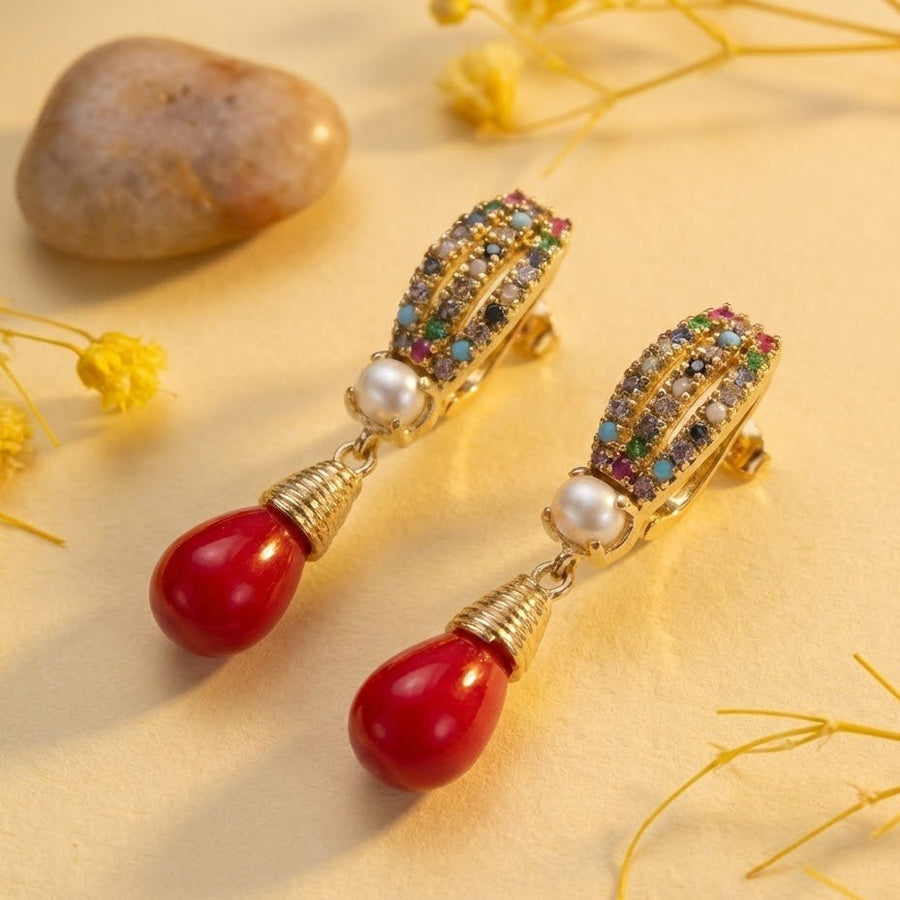 Gold-tone multicolor crystal and pearl drop earrings showcased with natural stone and yellow flowers background